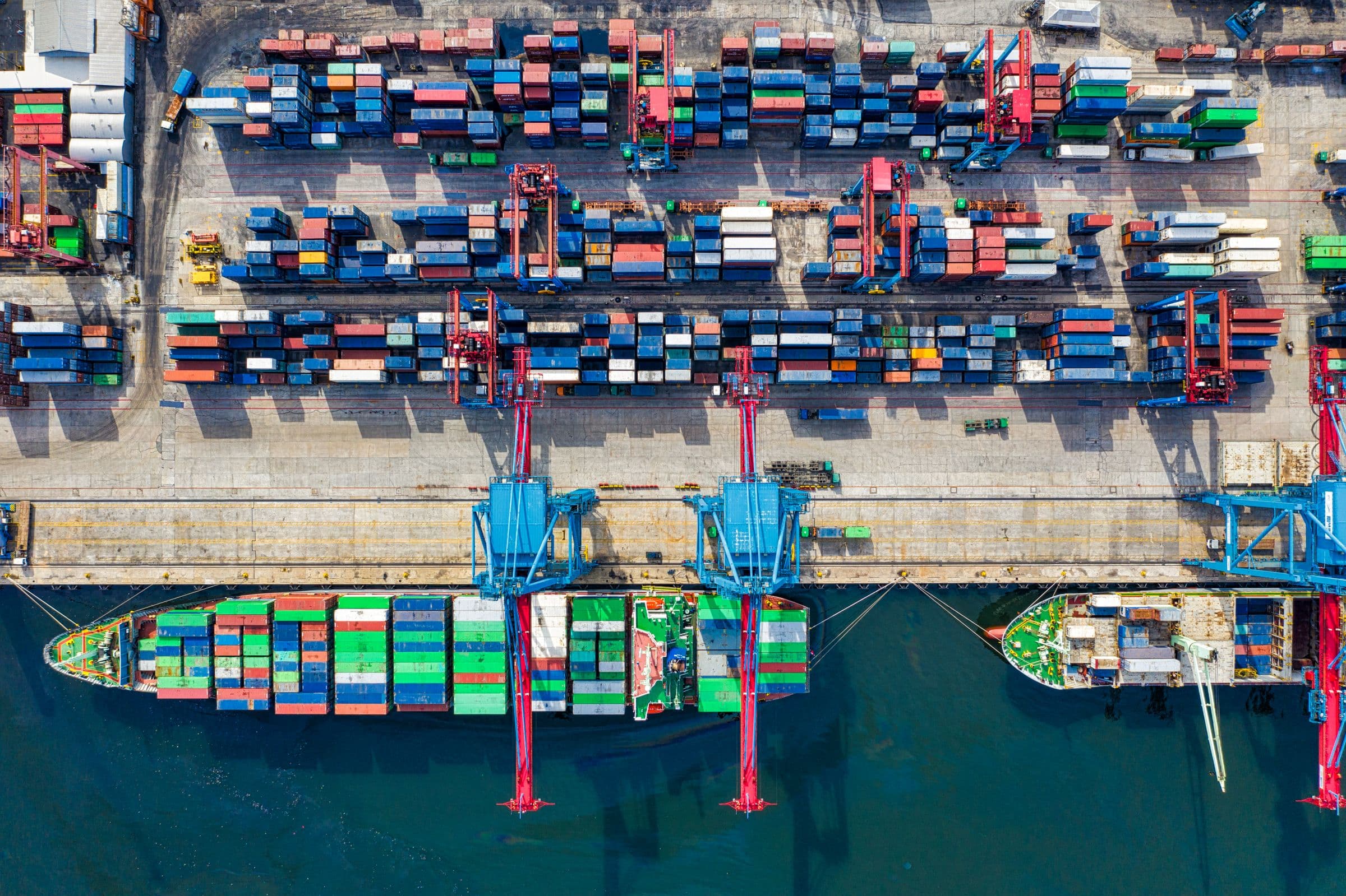 Aerial view of a container terminal, with a cargo vessel loading beneath ship-to-shore cranes